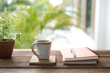 Vintage ceramic coffee cup and notebooks and plant pot on brown wooden table
