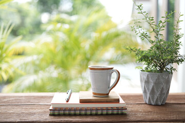 Vintage ceramic coffee cup and notebooks and plant pot on brown wooden table