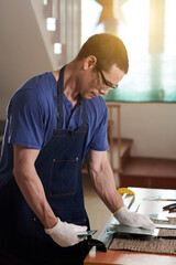 Vertical image of craftsperson in apron using lathe to cut glass during his work in workshop