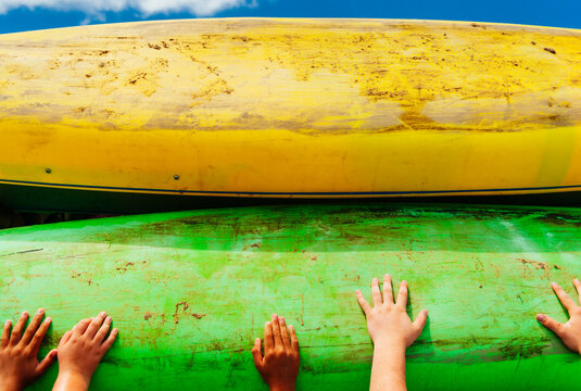 Children's hands push a kayak into place on a roof rack