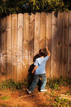 A small boy draws on a new wooden fence with white chalk