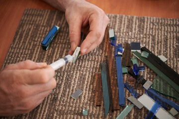 Close-up of professional glassworer glueing colored glass sitting at his workplace