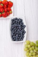 Strawberries, blueberry and grapes in white ceramic plates on a wooden table.  Fresh and healthy food concept. Raw vegetarian food.