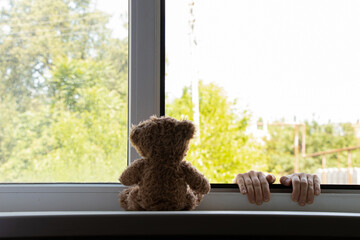 Children's hands hold on to the window from the side of the street and a teddy bear sits on the...