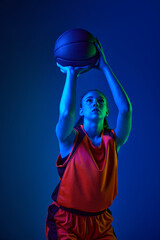 Winning goal. Young girl, concentrated basketball player throwing ball against blue studio...