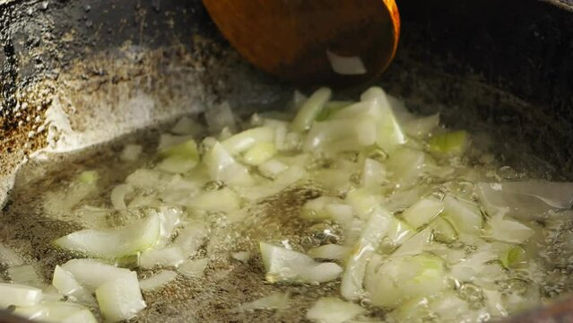 Finely chopped onion fried in a frying pan with asl is mixed with a wooden spatula. Close-up