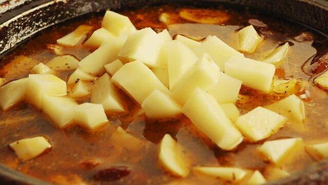 Sliced potatoes fall into the cholnt chicken and potatoes in spices. close-up