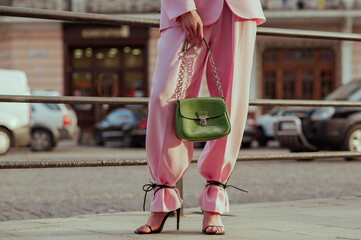 Street fashion details: woman wearing trendy pink suit trousers, high heeled strap sandals, carrying green color faux reptile leather bag. Copy, empty space for text
- 613965604