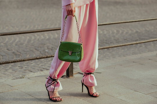 Street fashion details: woman wearing trendy pink suit trousers, high heeled strap sandals, carrying green color faux reptile leather bag. Copy, empty space for text
