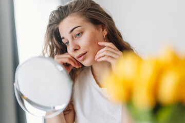 oung woman with problem skin looking into mirror. Dermatology. Allergic reaction from cosmetic, red...