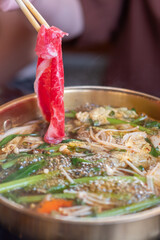 Chopstick holding sliced meat. hot pot with thick soup.