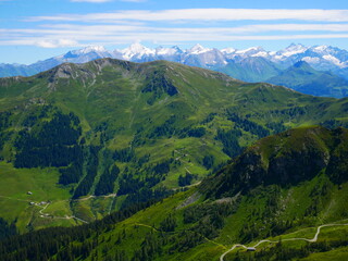 Fototapeta premium View on mountains near Saalbach Hinterglemm ski resort on a summer day,green meadows,mountains, blue sky, clouds, Hohen Tauern mountains with glaciers in background. Alps, Austria. .