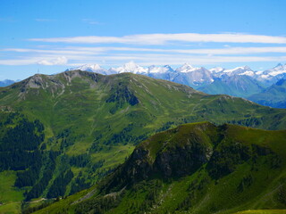 Obraz premium View on mountains near Saalbach Hinterglemm ski resort on a summer day,green meadows,mountains, blue sky, clouds, Hohen Tauern mountains with glaciers in background. Alps, Austria. .