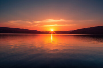 A breathtaking sunset over a serene lake, with vibrant hues reflecting on the calm water, creating a peaceful and captivating atmosphere