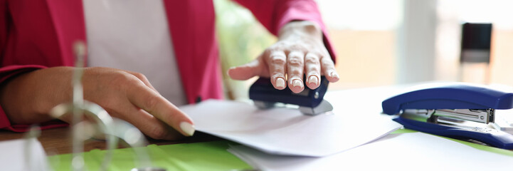 Female hands punching holes with puncher in documents in office