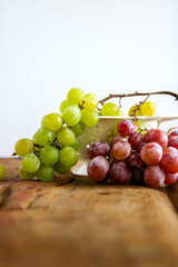 Assortment of ripe sweet grapes in a vintage strainer over wooden surface and white background