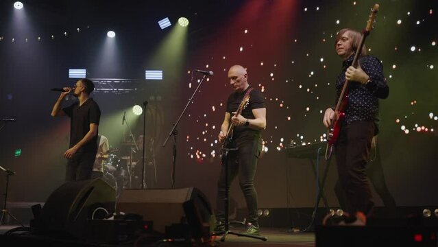 Band with three guitarists and singer performs at concert in nightclub. Spotlights. Live concert. Slow motion