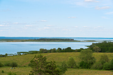 Panoramic view of the river bank with flood meadows. In the meadow, a group of people are picking wild strawberries.