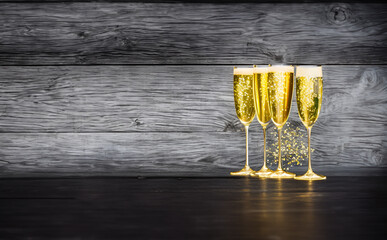 Champagne glasses with golden glitter on black wooden background
