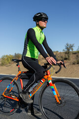 Obraz premium Cyclist riding bicycle on road against clear sky. A man in an outfit stands with a bicycle on an autumn sunny day.
