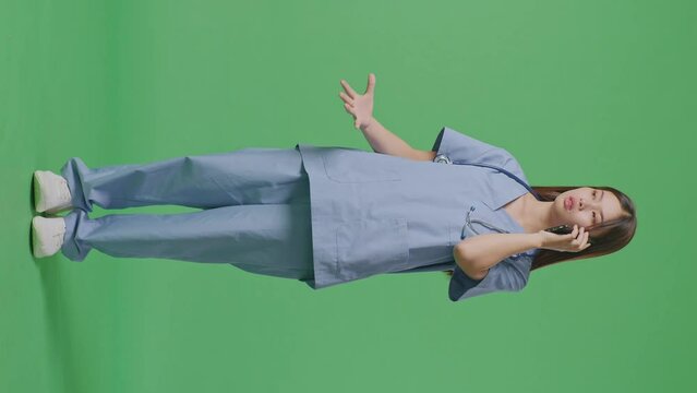 Full Body Of Asian Female Doctor With Stethoscope Shouting On Smartphone While Standing On Green Screen Background In The Hospital
