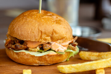 Tasty home made burger served with crispy fries. Rustic hamburger and potato chips composition with baking paper and wooden table