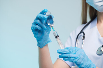The doctor's hand wears a medical glove holding a syringe while taking a liquid vaccine from a vial...