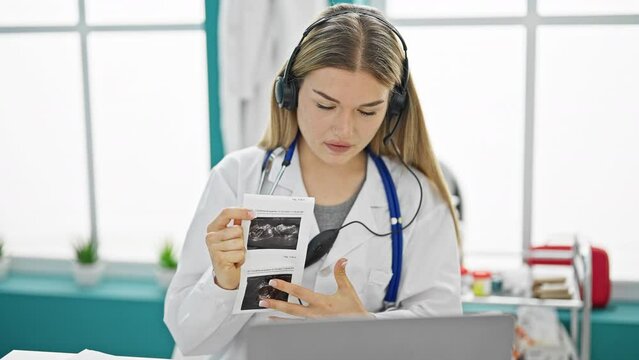Young blonde woman doctor on video call showing baby ultrasound at clinic