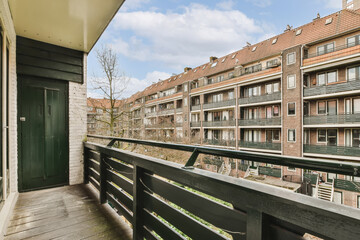 a balcony with some buildings in the background and a green door on the right hand side that leads to an apartment