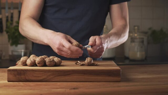 A man shelling walnuts with a steel nutcracker over a wooden surface.