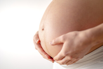 Pregnant woman gently holding her naked round belly with her hands in final month of pregnancy. Third trimester - week 36. Close up. Side view. White background. Bright shot.