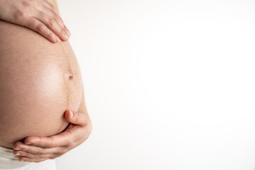 Pregnant woman gently holding her naked round belly with her hands in final month of pregnancy. Third trimester - week 36. Close up. Side view. White background. Bright shot.