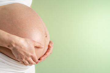 Pregnant woman gently holding her naked round belly with her hands in final month of pregnancy....