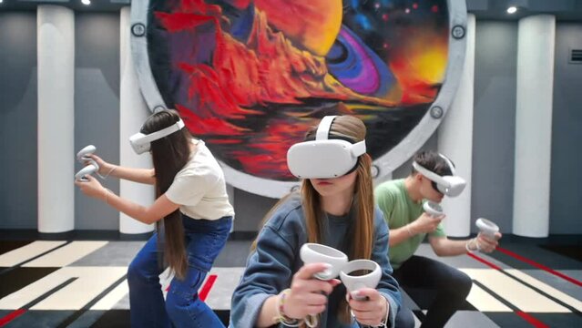 Group of three teens with VR headset and controllers playing games in a team on a VR arena. Slow motion