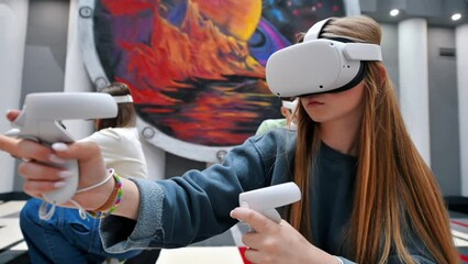 Group of three teens with VR headset and controllers playing games in a team on a VR arena, sitting and aiming. Slow motion