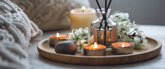 Aromatherapy, cozy atmosphere. Home perfume in glass bottle with wooden sticks, scented burning candles. Light spring cherry apple blossom fragrance, fresh flowers. Banner