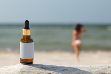 Natural sun defense concept. Dropper bottle on the beach. Blurred silhouette of a woman, the...