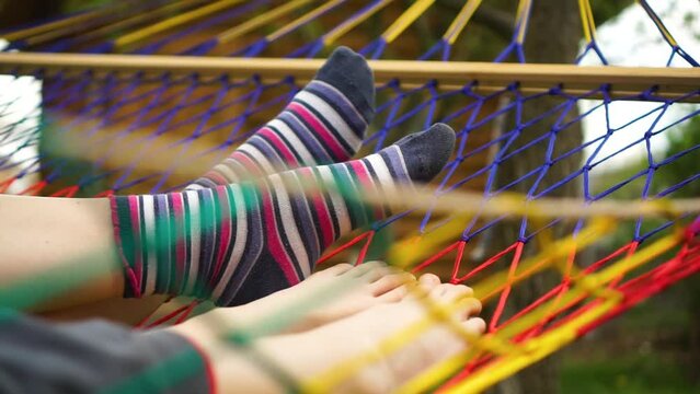 Two pair of feet in colorful funny socks hanging in hammock during summer time. Mother child chilling together