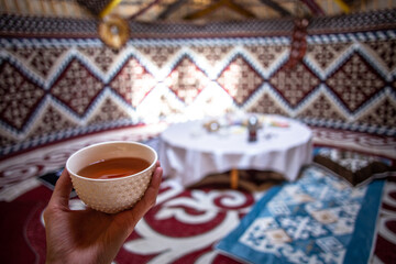 a cup of tea in a man's hand behind a dastarkhan in the Kazakh national yurt