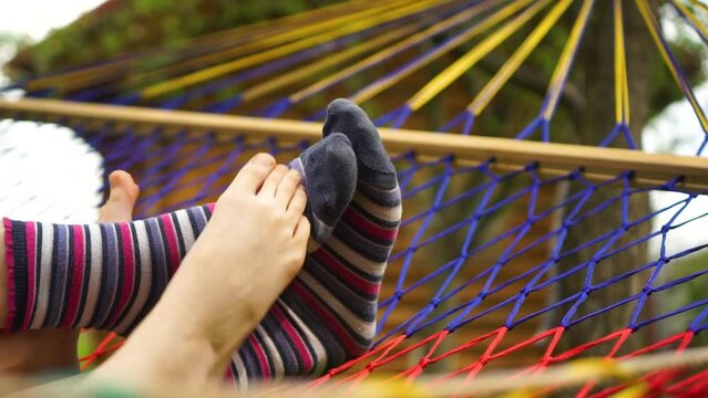 Two pair of feet one in colorful socks hanging in hammock during summer time. Mother child chilling together
