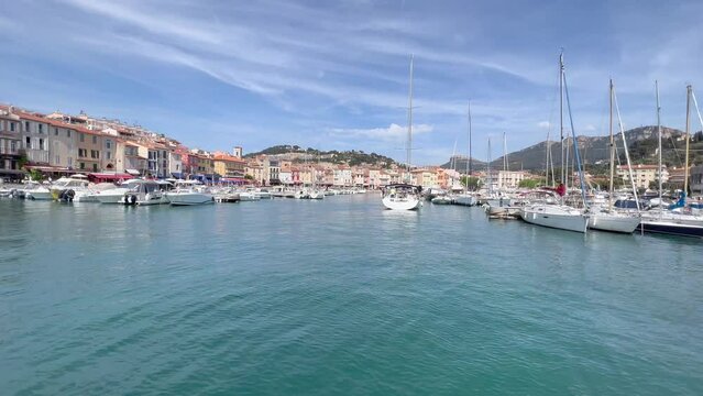 Port of Cassis. Marina, quay full of yachts and boats. View from a moving boat which arrives at harbour. Colourful French Riviera houses in the background.  Cassis, Cote d'Azur, France
