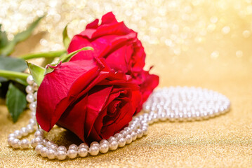 Red rose and pearl necklace on a shiny gold background
