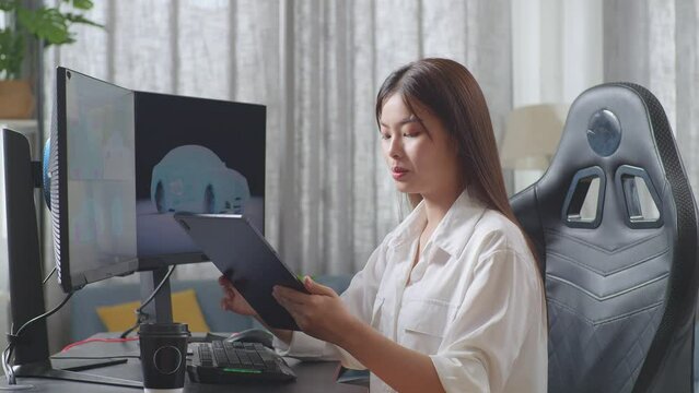 Side View Of Asian Female Automotive Designer Comparing The 3D Model Of Ev Car On The Desktop Computers To The Photo On Her Tablet In The Studio
