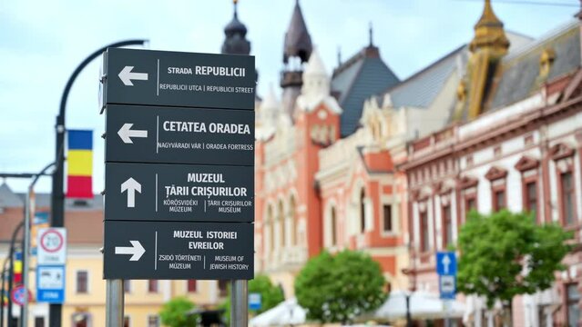 View of a sign showing directions to popular places on the Unirii Square with multiple old buildings made in classic style on the background in Oradea, Romania