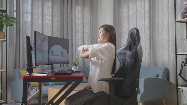 Side View Of Asian Female Automotive Designer Stretching While Working On 3D Model Of Ev Car On The Desktop Computers In The Studio
