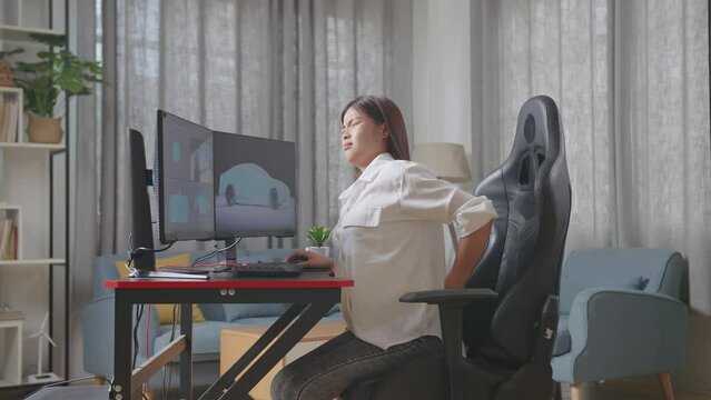 Side View Of Asian Female Automotive Designer Having A Backache While Working On 3D Model Of Ev Car On The Desktop Computers In The Studio
