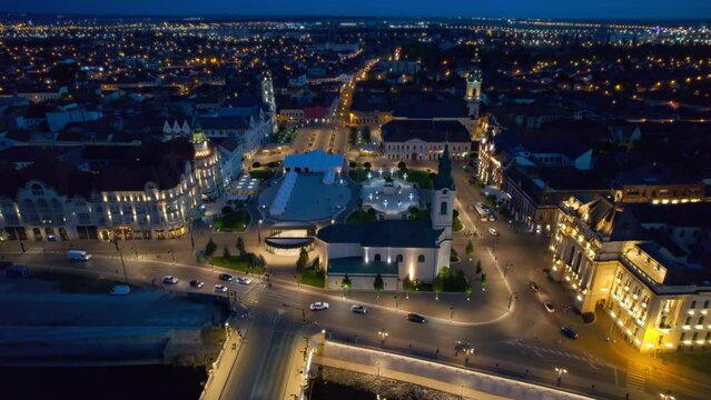 Areal drone view of the Unirii Square in Oradea downtown at night, Romania. King Ferdinand I statue, Saint Ladislaus Church, Town Hall and other historical buildings, illumination