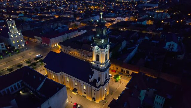 Areal drone view of the Unirii Square in Oradea downtown at night, Romania. Cathedral of St. Nicholas, illumination, multiple buildings around