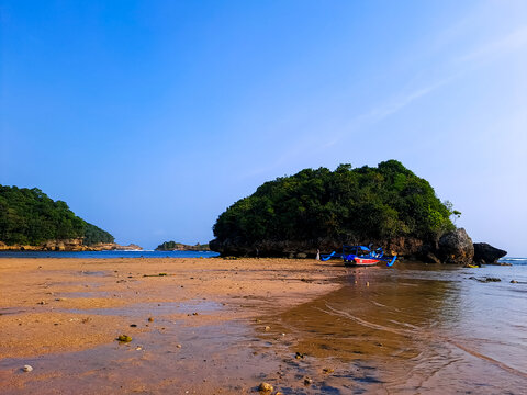 Low tidewater in a beautiful beach with sand, rocks and green vegetation under clear blue sky during a summer vacation. Kondang Merak Beach, Malang, Indonesia