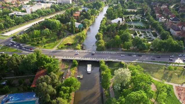 Aerial drone view of Bega river in Timisoara, Romania. View of the river with floating boat, greenery on the both sides of the river and bridge with moving cars, cityscape